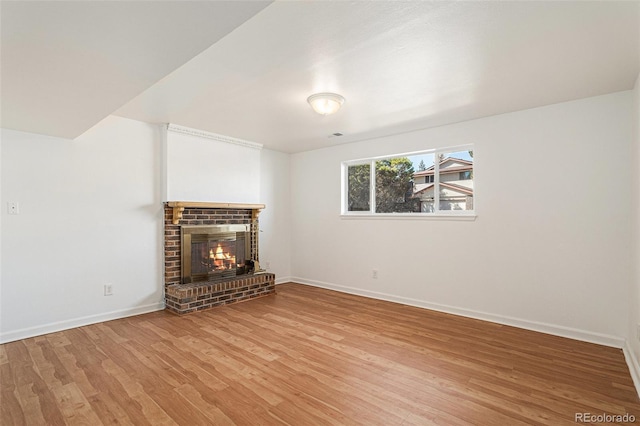 unfurnished living room with a brick fireplace, wood finished floors, and baseboards