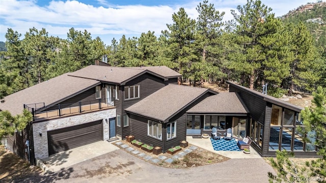 view of front of home featuring aphalt driveway, a patio area, an attached garage, stone siding, and a shingled roof