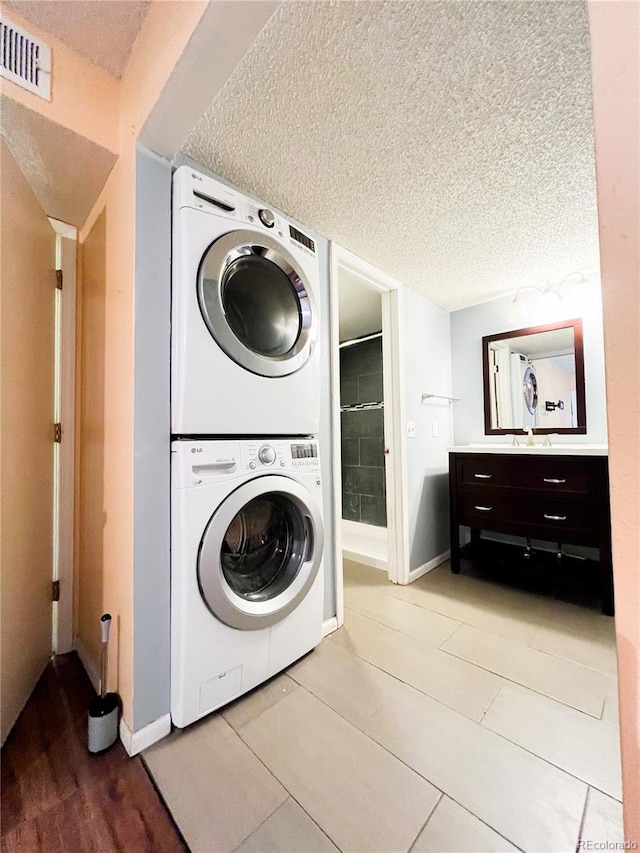 clothes washing area with light tile patterned floors, sink, a textured ceiling, and stacked washing maching and dryer