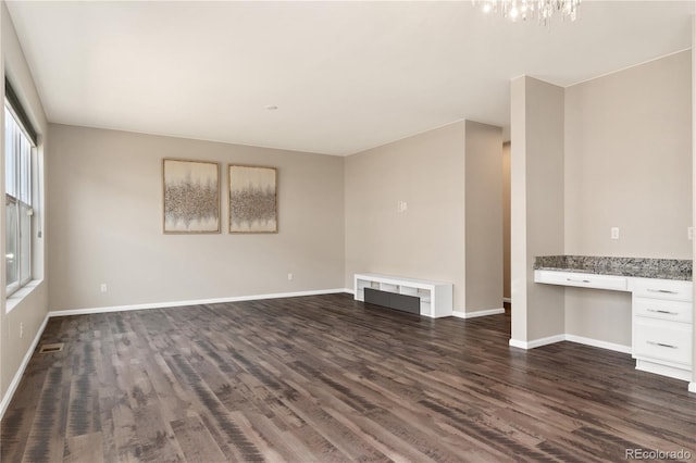 unfurnished living room with dark hardwood / wood-style floors, built in desk, and a notable chandelier