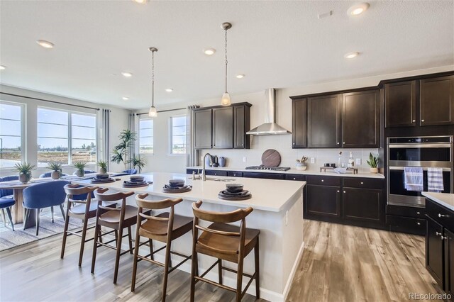 1320 Loraine Cir N, Lafayette, CO 80026 - kitchen featuring wall chimney range hood, appliances with stainless steel finishes, a sink, light countertops, and a center island with sink