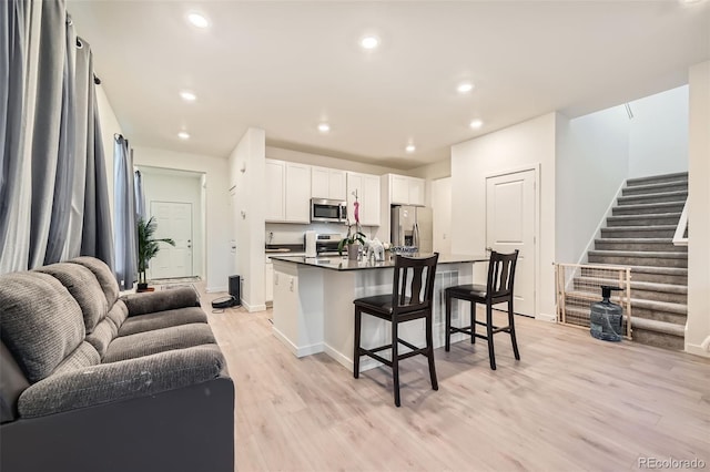 kitchen with a kitchen breakfast bar, white cabinets, light wood-type flooring, a center island with sink, and stainless steel appliances