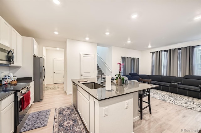 kitchen with appliances with stainless steel finishes, white cabinetry, sink, a breakfast bar, and an island with sink