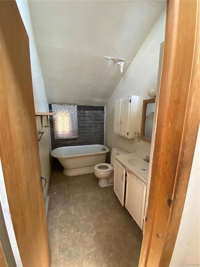 bathroom featuring vaulted ceiling, a bath to relax in, tile floors, toilet, and vanity