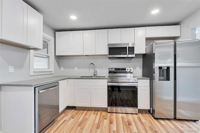 kitchen with appliances with stainless steel finishes, light wood-style floors, white cabinetry, a sink, and recessed lighting