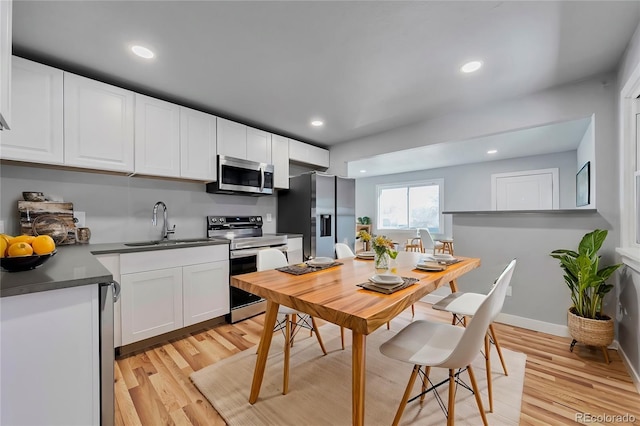 kitchen with dark countertops, light wood-style floors, appliances with stainless steel finishes, and white cabinets