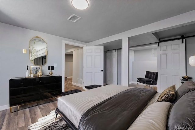 bedroom with a barn door, wood finished floors, visible vents, and baseboards