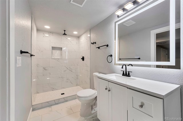 bathroom featuring visible vents, toilet, marble finish floor, a tile shower, and vanity