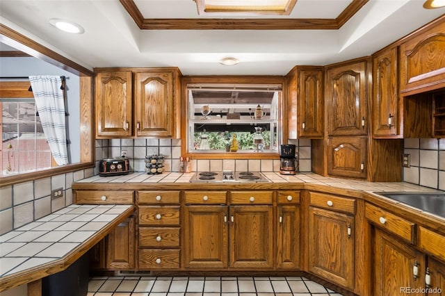 kitchen featuring backsplash, a tray ceiling, crown molding, white stovetop, and tile countertops