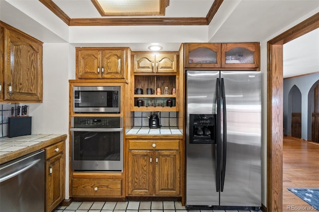 kitchen with tile countertops, ornamental molding, and appliances with stainless steel finishes