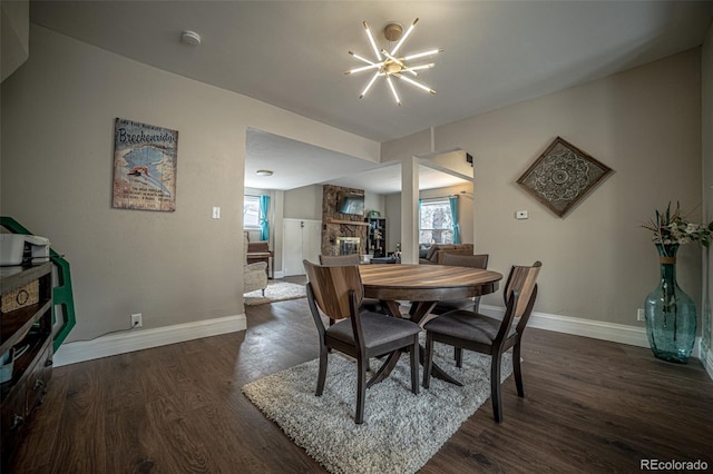 dining space featuring an inviting chandelier, plenty of natural light, dark hardwood / wood-style flooring, and a stone fireplace