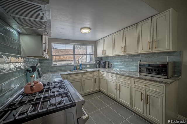 kitchen featuring sink, white cabinetry, stainless steel range with gas stovetop, dark tile patterned floors, and light stone countertops