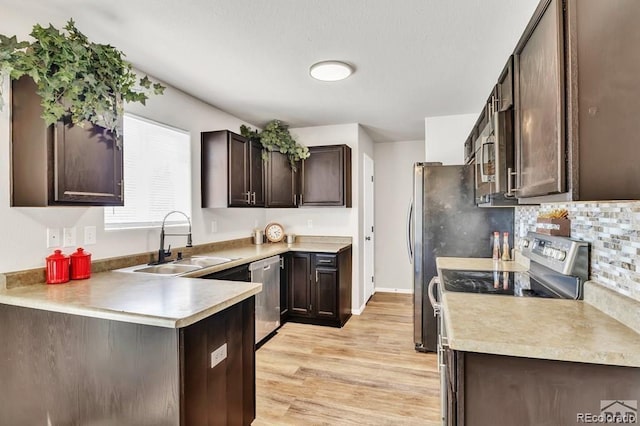 kitchen featuring sink, kitchen peninsula, light wood-type flooring, dark brown cabinets, and appliances with stainless steel finishes