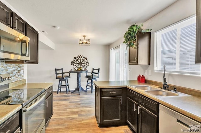 kitchen featuring sink, kitchen peninsula, light hardwood / wood-style floors, dark brown cabinets, and appliances with stainless steel finishes