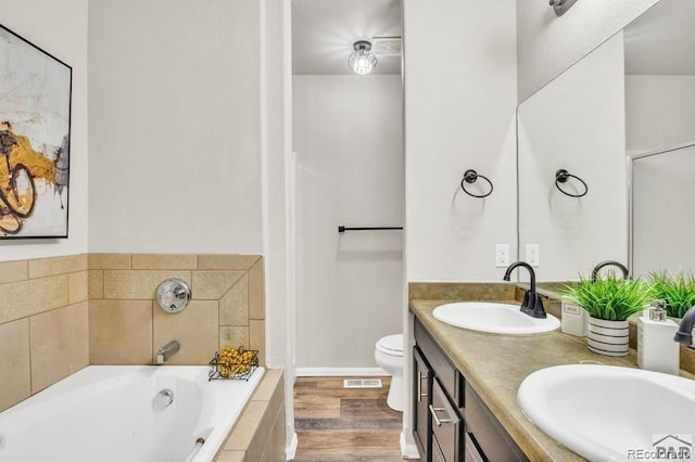 bathroom with hardwood / wood-style floors, vanity, toilet, and tiled bath