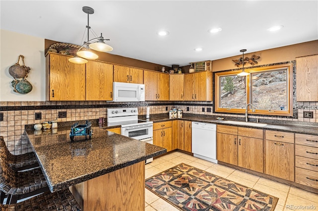 kitchen with white appliances, a peninsula, a kitchen bar, pendant lighting, and a sink