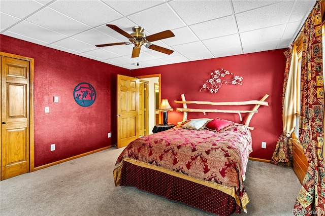 carpeted bedroom with ceiling fan, a drop ceiling, and baseboards