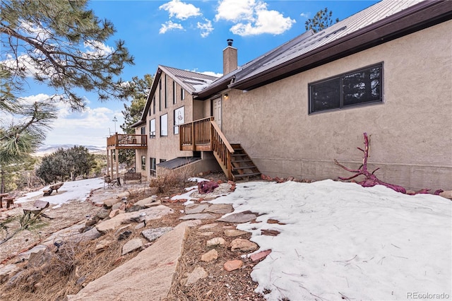 view of side of property featuring stairway, stucco siding, a chimney, and a deck