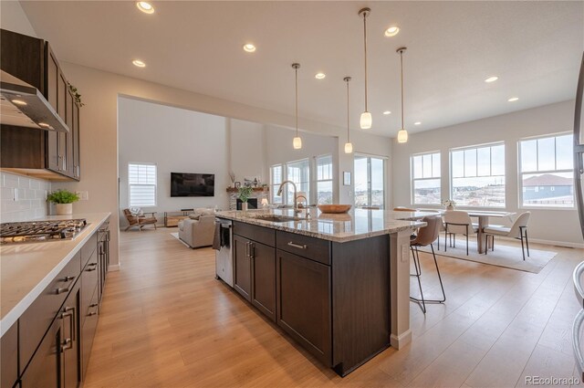 kitchen with dark brown cabinets, a breakfast bar, light wood finished floors, a sink, and appliances with stainless steel finishes