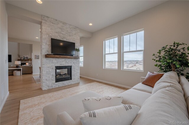living room with a stone fireplace, light wood-type flooring, baseboards, and recessed lighting