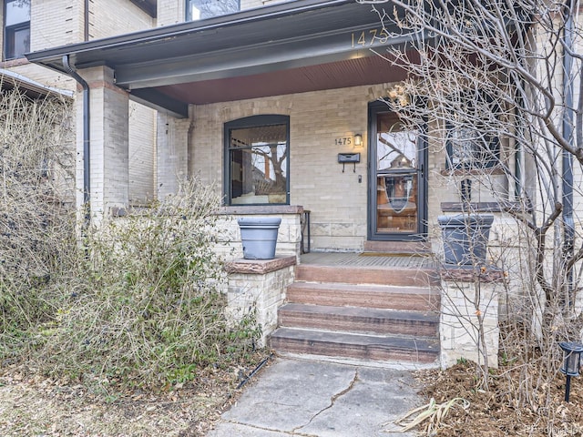 view of exterior entry with brick siding and a porch