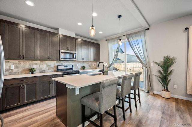 kitchen with hanging light fixtures, an island with sink, appliances with stainless steel finishes, dark brown cabinets, and sink