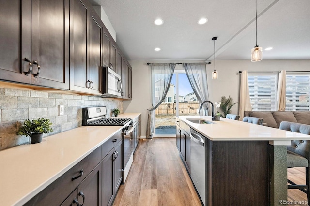 kitchen with sink, a kitchen breakfast bar, decorative backsplash, hanging light fixtures, and appliances with stainless steel finishes