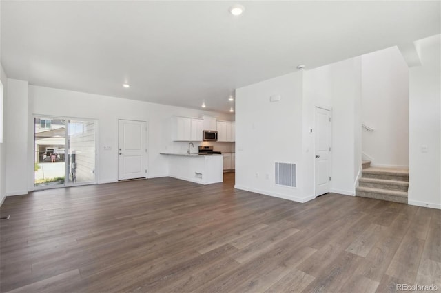 unfurnished living room with dark wood-type flooring, stairway, a sink, baseboards, and recessed lighting