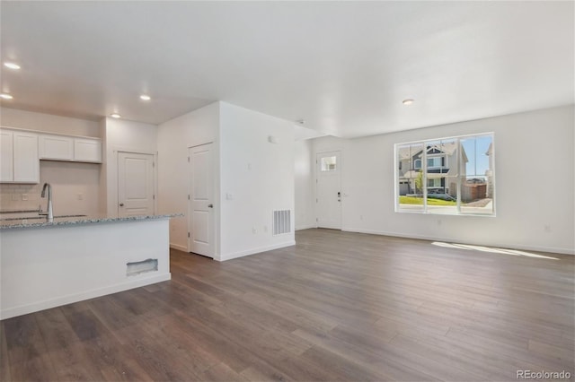 unfurnished living room with recessed lighting, dark wood finished floors, baseboards, and a sink