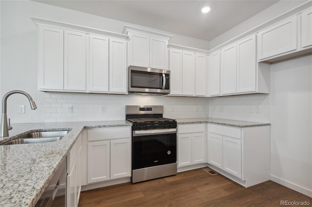 kitchen featuring appliances with stainless steel finishes, a sink, white cabinets, tasteful backsplash, and dark wood-style flooring