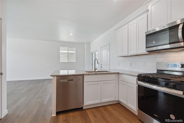 kitchen with stainless steel appliances, a sink, a peninsula, wood finished floors, and white cabinetry