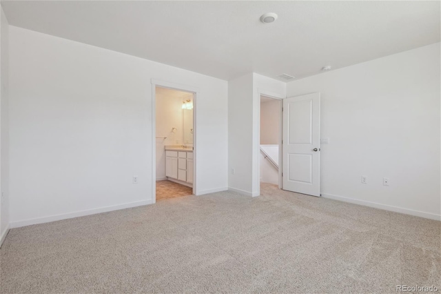 unfurnished bedroom with light colored carpet, baseboards, and ensuite bathroom