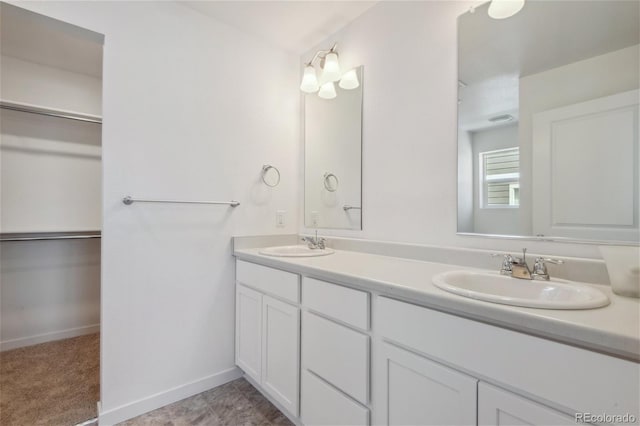 bathroom with double vanity, a walk in closet, and baseboards