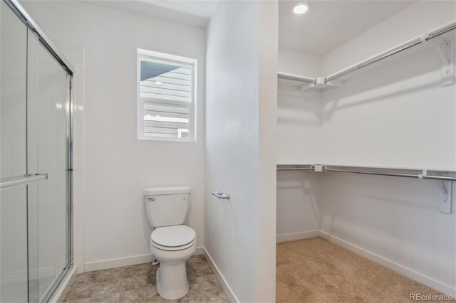 full bathroom with a walk in closet, a tile shower, toilet, and baseboards