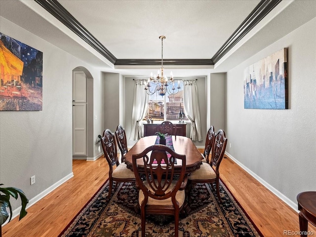 dining space featuring arched walkways, baseboards, light wood-style floors, ornamental molding, and a tray ceiling