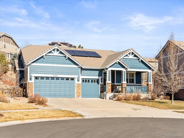 craftsman inspired home featuring a porch, roof mounted solar panels, a garage, driveway, and a tiled roof