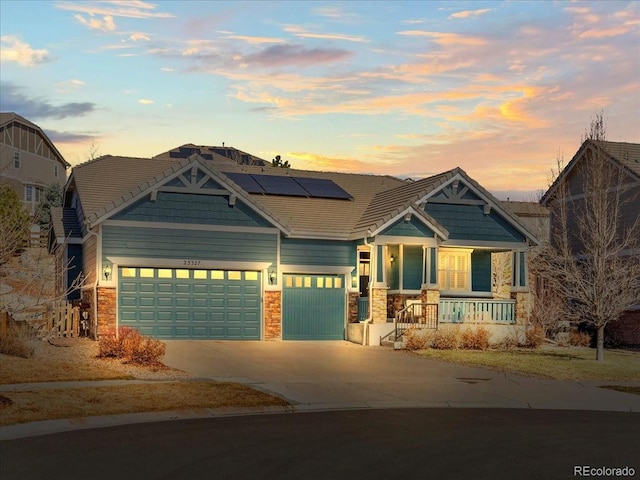 craftsman-style home featuring covered porch, an attached garage, roof mounted solar panels, stone siding, and driveway