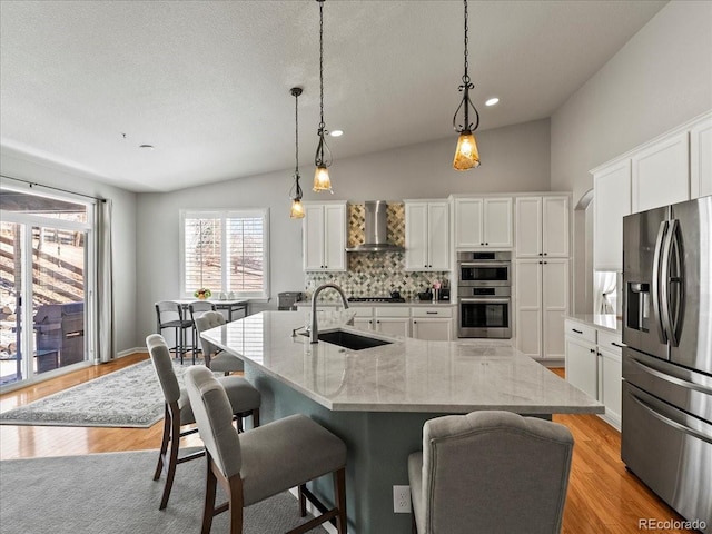 kitchen featuring lofted ceiling, a sink, white cabinets, appliances with stainless steel finishes, and wall chimney exhaust hood