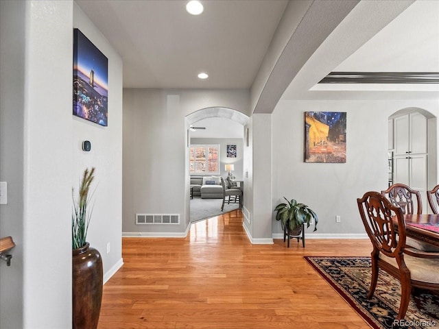 hallway featuring arched walkways, baseboards, visible vents, and light wood finished floors