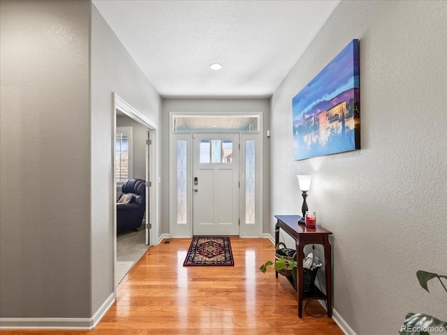 entryway featuring light wood-type flooring, baseboards, a textured ceiling, and a textured wall