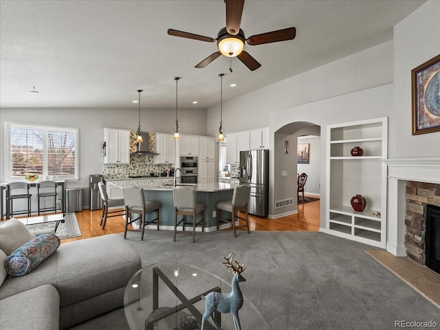 living room with built in features, arched walkways, lofted ceiling, visible vents, and a stone fireplace