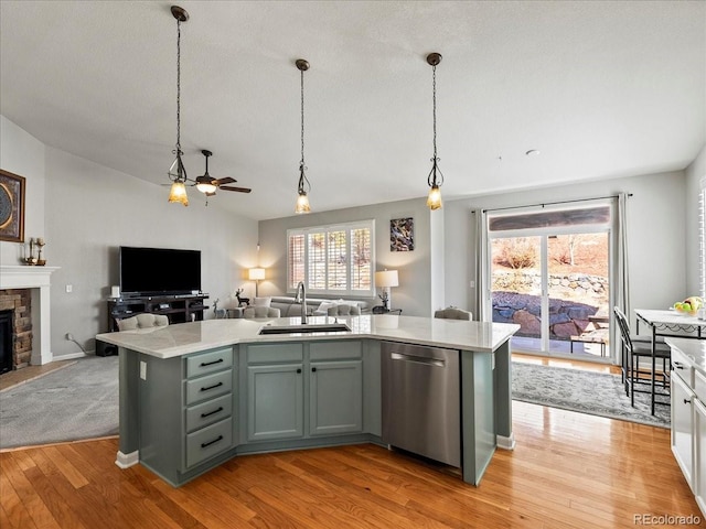 kitchen featuring open floor plan, light countertops, a stone fireplace, stainless steel dishwasher, and a sink