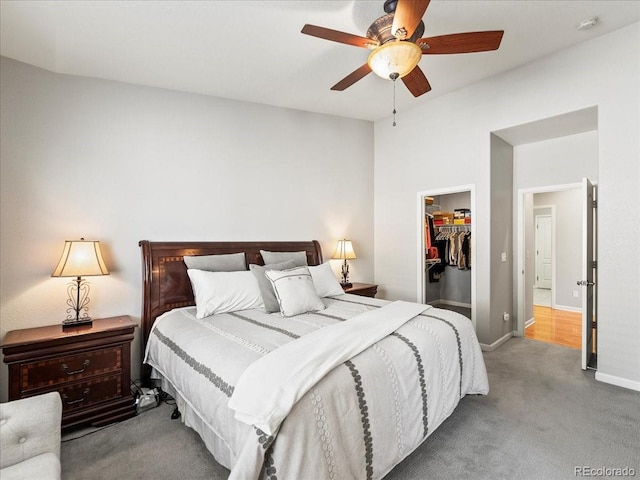 carpeted bedroom with a ceiling fan, baseboards, a walk in closet, and a closet