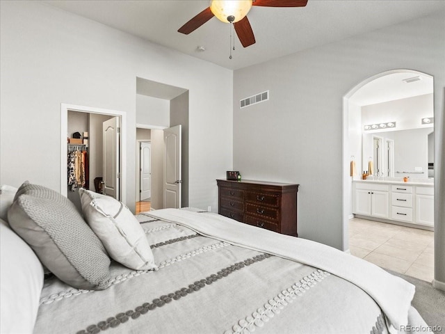 bedroom with arched walkways, ensuite bathroom, visible vents, vaulted ceiling, and a walk in closet