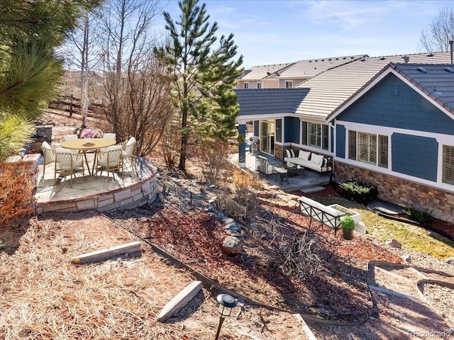 rear view of house featuring a tile roof, stone siding, and a patio area