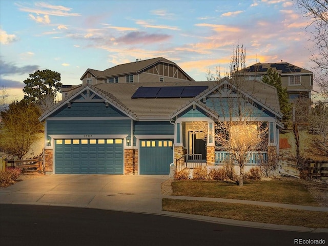 craftsman-style house featuring stone siding, roof mounted solar panels, an attached garage, and concrete driveway