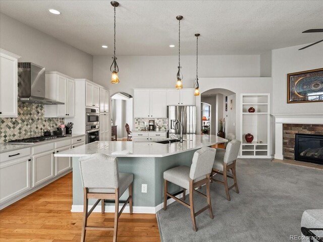 23327 E Ottawa Dr, Aurora, CO 80016 - kitchen with wall chimney exhaust hood, arched walkways, appliances with stainless steel finishes, white cabinetry, and a kitchen breakfast bar