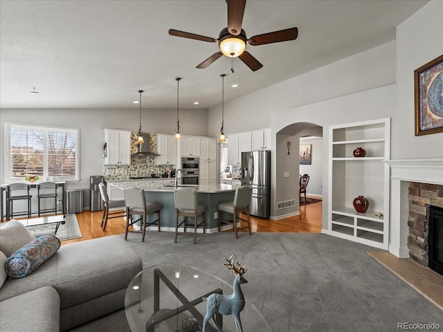 23327 E Ottawa Dr, Aurora, CO 80016 - living room featuring arched walkways, lofted ceiling, a ceiling fan, built in shelves, and a stone fireplace