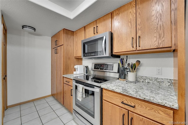 kitchen featuring light tile patterned floors, light stone countertops, a textured ceiling, and appliances with stainless steel finishes