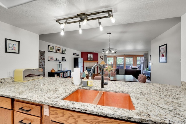 kitchen with sink, hanging light fixtures, light stone counters, a textured ceiling, and a tiled fireplace